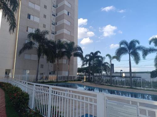a swimming pool in front of a building with palm trees at Residencial Vitrine Esplanada in Votorantim