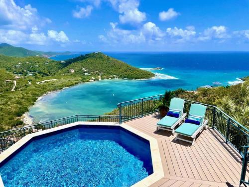 a swimming pool with two chairs and the ocean at Windsong Villa - Sleeps 8 Stunning Views in Cruz Bay