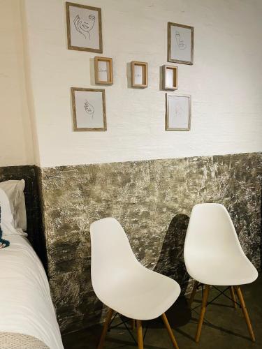 2 chaises blanches assises à côté d'un mur avec des photos dans l'établissement Golden Maboneng, à Johannesbourg