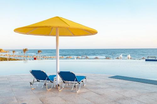 two chairs under a yellow umbrella next to a pool at Pickalbatros Vita Resort - Portofino Marsa Alam in Abu Dabab