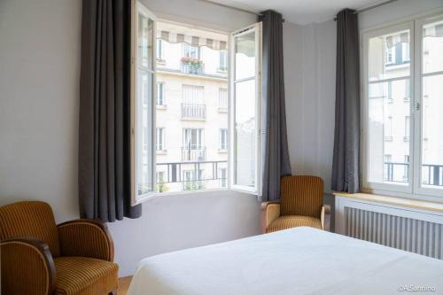 - une chambre avec deux chaises, un lit et deux fenêtres dans l'établissement Moderne 2 pièces en plein Paris au bord de Seine, à Paris