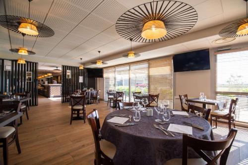 uma sala de jantar com mesa, cadeiras e janelas em Brit Hotel & Spa Côte des Sables em Plouescat
