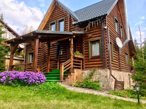 una cabaña de madera con flores púrpuras delante de ella en Cottage PolyaNitsa окремий котедж з каміном en Bukovel