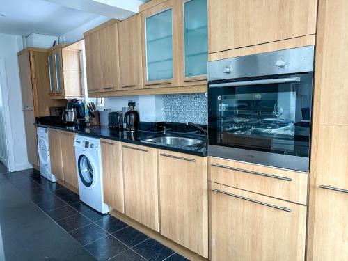 a kitchen with wooden cabinets and a sink and a dishwasher at Modern four bedroom semi-detached house with off street parking 8 min drive to Wembley stadium, 5 miles to Central London in London
