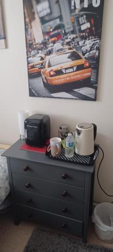 a black dresser with two cups and a picture of a race car at Aylesbury Lovely Double and Single Bedroom with Guest only Bathroom in Buckinghamshire