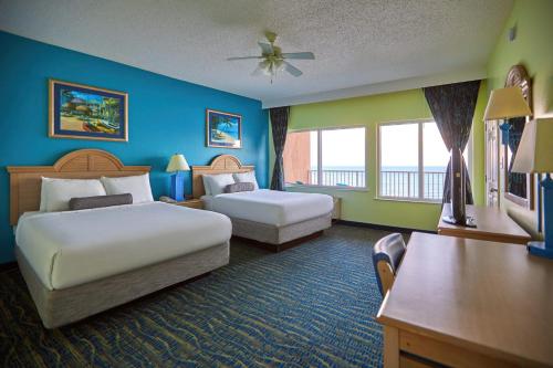 a hotel room with two beds and a desk at Palmetto Beachfront Hotel, a By The Sea Resort in Panama City Beach