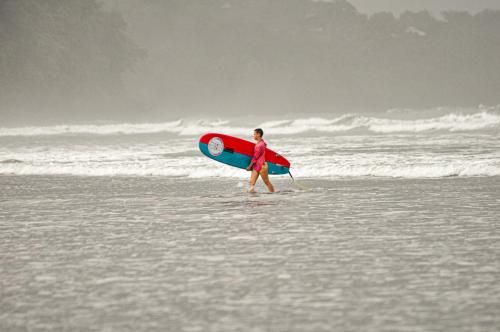 a woman walking on the beach with a surfboard at Nomadic Surf Camp in Uvita