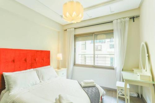 a white bedroom with a red headboard and a window at Résidence Massira Square Place in Casablanca