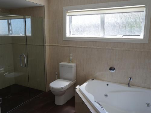 a bathroom with a toilet and a tub and a window at Luxury Palms in Paihia