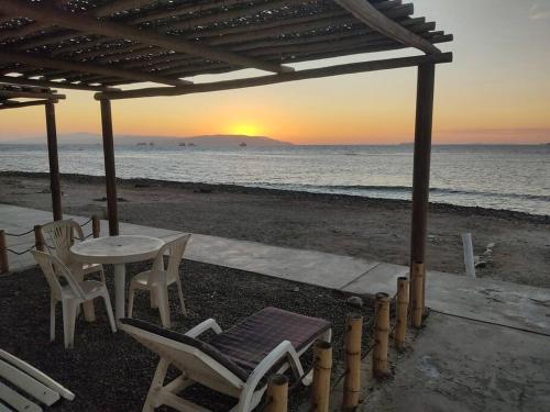 Beach House SantaElena في بيسكو: طاولة وكراسي على الشاطئ مع غروب الشمس