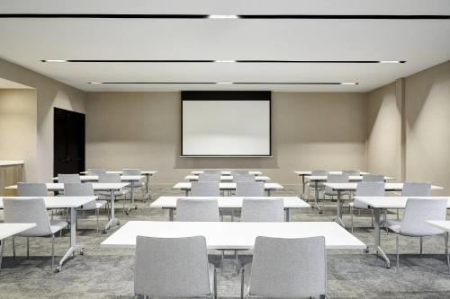 a classroom with white tables and chairs and a screen at AC Hotel by Marriott Tampa Airport in Tampa