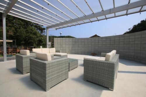 a patio with wicker chairs and a pergola at Sloth Glamping in Izumi