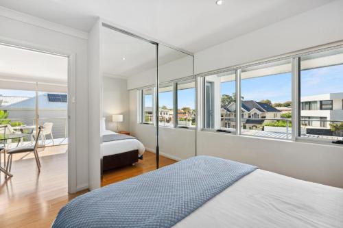 a bedroom with a bed and a table and windows at Applecross Riverside Apt in Perth