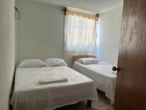 a bedroom with two beds with white sheets and a window at Casa Costa Del Sol in Puerto Escondido