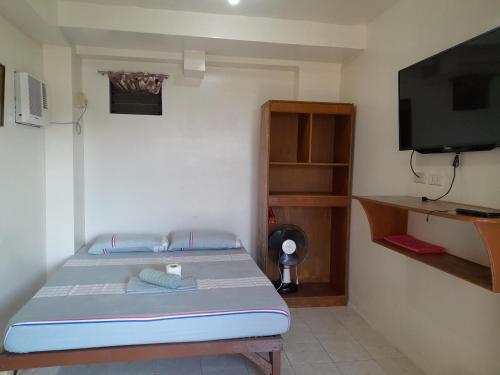 um pequeno quarto com uma cama e uma televisão em Reynaldo's Upstairs em Puerto Galera