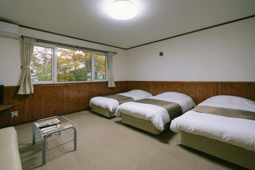a room with four beds and a table in it at Pension Ashitaya in Furano