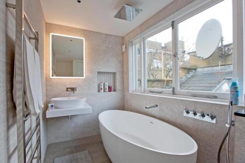 a bathroom with a white tub and a sink and a window at 2-Bed Gem near Harrods: Prime Location in London
