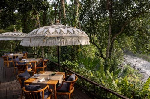a restaurant with tables and umbrellas on a deck at Mandapa, a Ritz-Carlton Reserve in Ubud