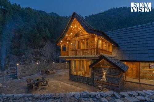 a log cabin with a balcony and a table at StayVista at Wisteria Whispers with Bonfire & River View in Gushaini