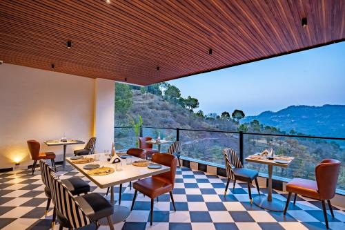 a restaurant with tables and chairs and a large window at Velmore Kasauli Operated by Royal Orchid Hotel Ltd. in Kasauli