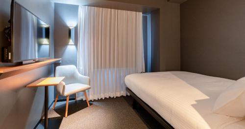a bedroom with a bed and a chair and a television at Grids Premium Hotel Kumamoto in Kumamoto