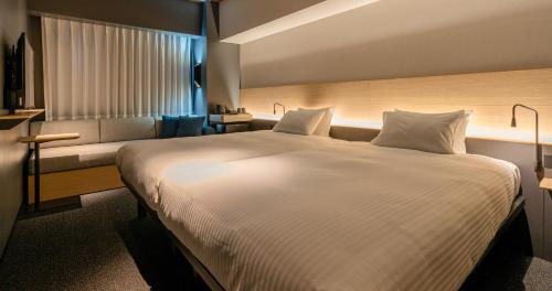 a bedroom with a large white bed and a couch at Grids Premium Hotel Kumamoto in Kumamoto