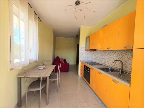 cocina con armarios naranjas, mesa y fregadero en Appartamento con tutti i confort, en Castro di Lecce
