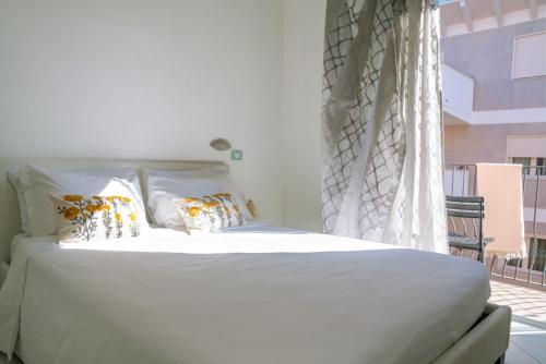 a bed with white sheets and pillows next to a window at Mare Home Brunch&Beauty - Adults Only in Cesenatico
