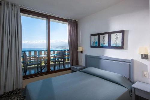 een slaapkamer met een bed en uitzicht op de oceaan bij Hersonissos Village Hotel & Bungalows in Chersonissos