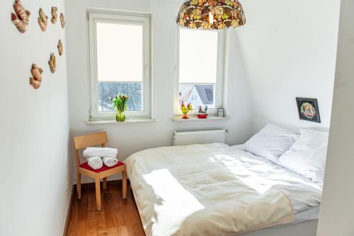 a white bedroom with a bed and two windows at Apartament Wiosenny in Szczecinek