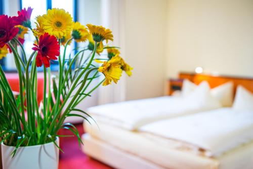 eine Vase voller Blumen auf einem Tisch neben einem Bett in der Unterkunft Hotel zum Ritter in Fulda