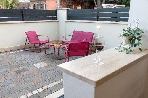 2 Stühle und ein Tisch mit Weingläsern auf der Terrasse in der Unterkunft KAMCHŪ RESIDENCE - VIA DEI LAGHI: APT #R2 in Ciampino