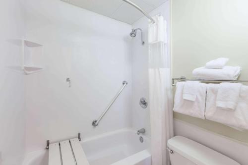 a white bathroom with a tub and a toilet and towels at Ramada Plaza by Wyndham Albany in Albany