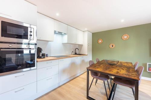 una cocina con armarios blancos y una mesa de madera con sillas. en Au Grès Des Vosges - 01, en Granges-sur-Vologne