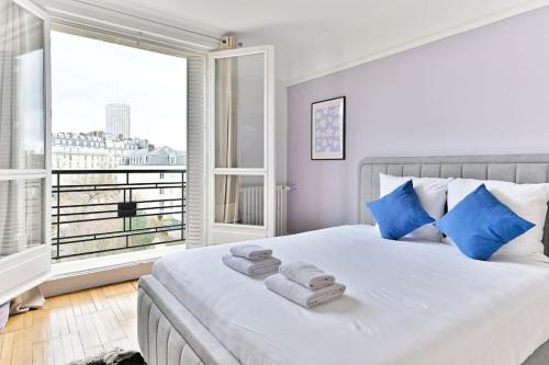 - une chambre dotée d'un lit blanc avec des oreillers bleus et d'une fenêtre dans l'établissement Appartement Luxueux Porte Maillot - Neuilly - IV, à Neuilly-sur-Seine