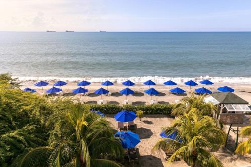 a beach with blue umbrellas and the ocean at Santa Marta Marriott Resort Playa Dormida in Santa Marta