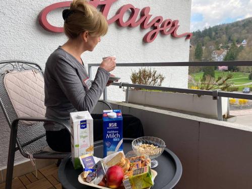 Hotel Harzer am Kurpark في باد هيرنالب: امرأة تجلس على شرفة مع طاولة من الطعام