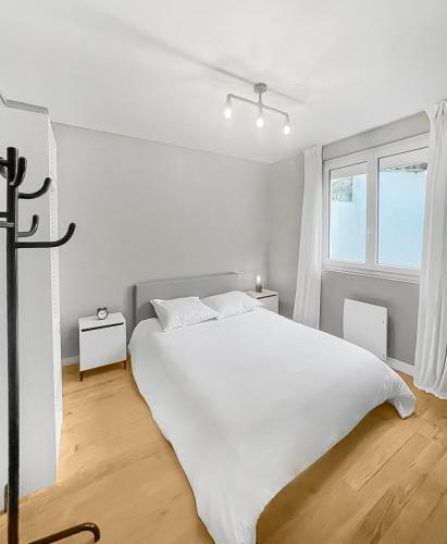 une chambre blanche avec un grand lit blanc et une fenêtre dans l'établissement L'Odyssée Nazairienne, à Saint-Nazaire