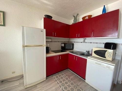 une cuisine avec des armoires rouges et un réfrigérateur blanc dans l'établissement T3 avec terrasse, ascenseur et parking au Barcarès près de la plage - FR-1-782-13, au Barcarès