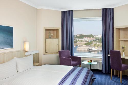 a hotel room with a bed and two chairs and a window at IntercityHotel Kiel in Kiel