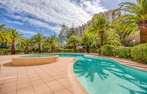 a swimming pool with palm trees and a building at Cozy Apartment In Mandelieu-La-Napoule in Mandelieu-la-Napoule