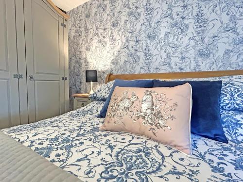 a bed with a blue and white comforter and a pillow at Lyndene Cottage in Moel-tryfan