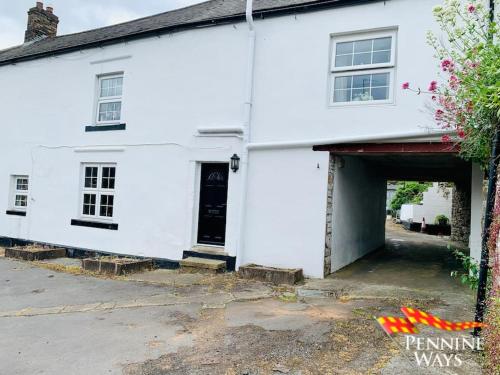 a white house with a garage in front of it at The Spotty - Homely Stay in a Former Inn in Haltwhistle