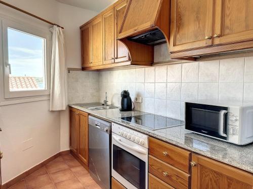 a kitchen with wooden cabinets and a sink and a microwave at F105 · Dos dormitorios, terraza y a/c en Fornells in Fornells