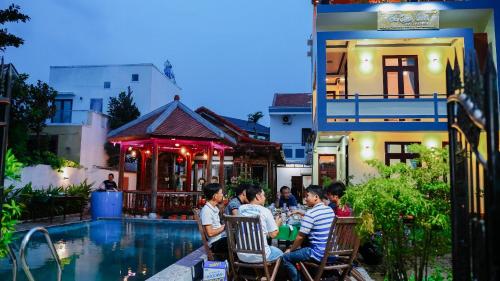 a group of people sitting around a table by a pool at Tra Que Green Villa Hoi An in Hoi An