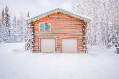 a log cabin with two garage doors in the snow at Tucked Away Timbers in Fairbanks