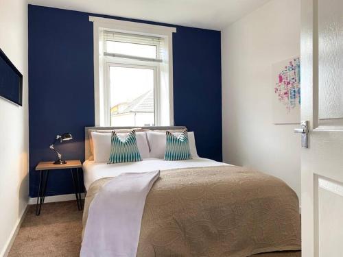 a bedroom with a bed with blue walls and a window at Modern And Vibrantly Designed Apartment in Motherwell
