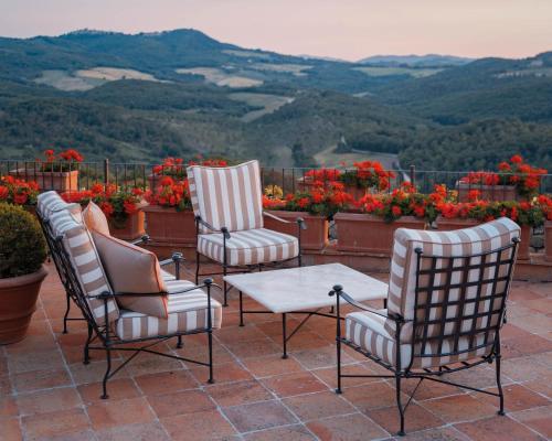 three chairs and a table on a patio with flowers at Castello di Casole, A Belmond Hotel, Tuscany in Casole dʼElsa