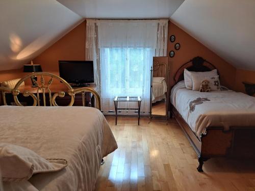 - une chambre avec 2 lits, une télévision et une fenêtre dans l'établissement Gîte au Charme Victorien, à Beauceville