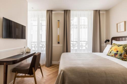 Habitación de hotel con cama, escritorio y TV. en Hôtel Chamar en París